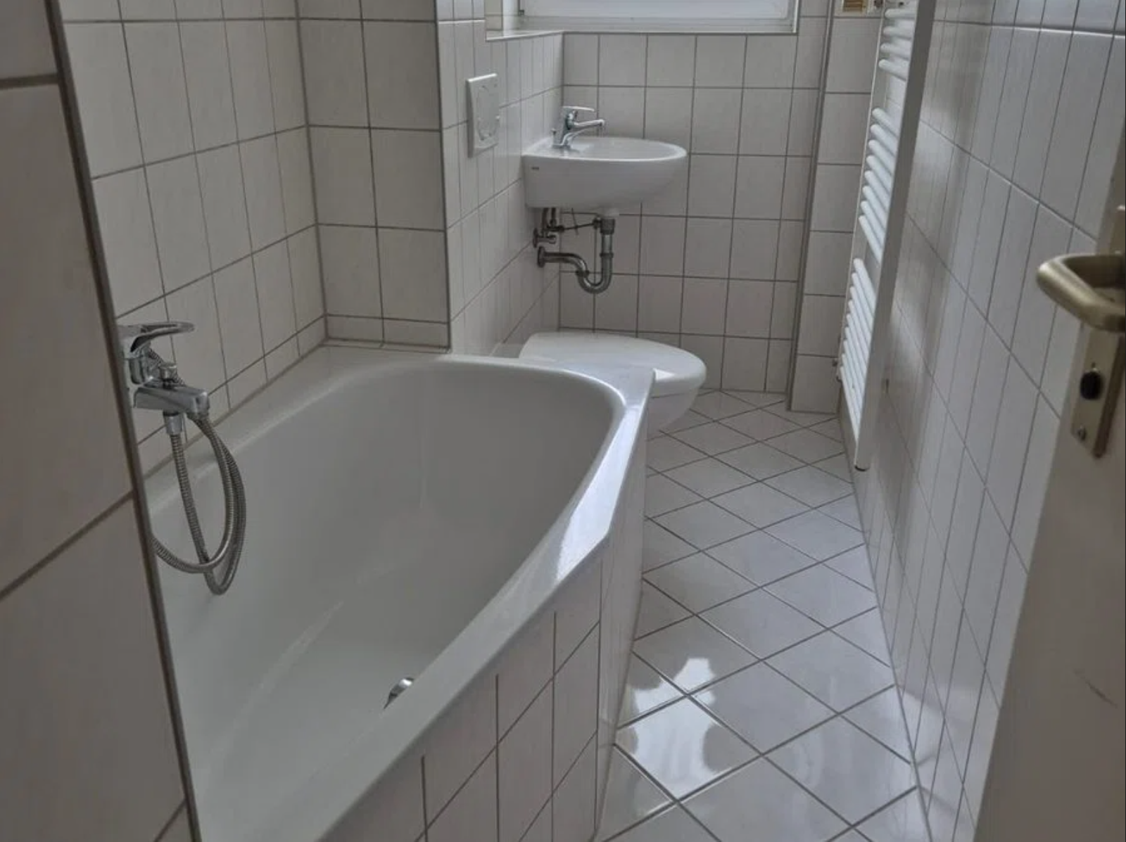 Sauberes weiß gefliestes Badezimmer mit Badewanne